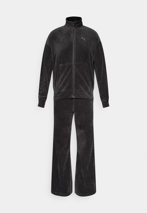 Tuta in corduroy grigio scuro con giacca con zip e pantaloni a gamba larga, caratterizzati da una leggera texture rigata e tasche frontali.