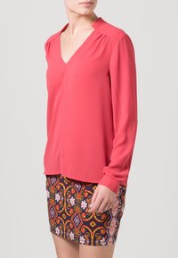 Růžová halenka s dlouhým rukávem a výstřihem do V, vyrobená z měkké látky, s nabíranými švy na ramenech, doplněná o vzorovanou mini sukni s květinovými a geometrickými motivy.