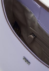 Jasnofioletowe wnętrze torebki z gładką teksturą, kieszonką na zamek błyskawiczny, podszewką z wytłoczonym wzorem DKNY.