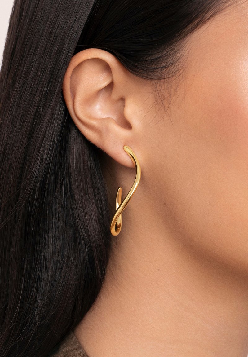 Boucles d'oreilles en métal doré avec un design fluide et sculptural comportant deux éléments courbes. La texture lisse et la finition brillante accentuent la forme.