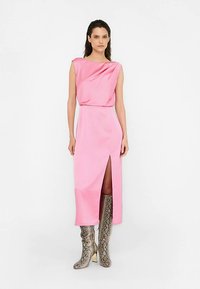 Roosa satiinist kleit kõrge lõhiku, ümar-kaeluse ja varrukateta disainiga. Koos metallikust madude mustriga põlveni ulatuvate saabastega.