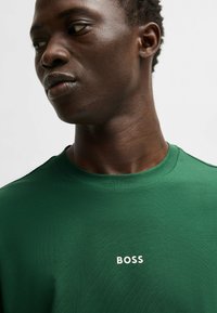 Grønn bomull T-skjorte med rund hals og korte ermer. Har en hvit "BOSS" logo på brystet. Glatt tekstur, avslappet design.