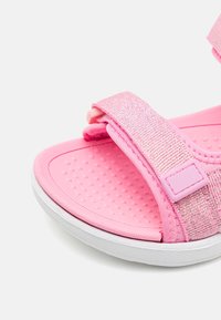 Różowe sandały z teksturowanymi, błyszczącymi paskami, z zapięciem na rzepy oraz wyściełaną wkładką. Posiadają białą gumową podeszwę i wzór w kropki.