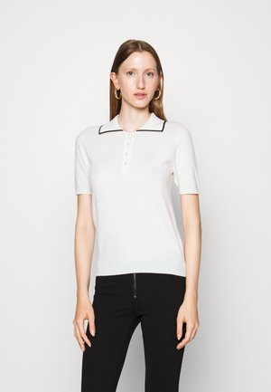 Hvid kortærmet polo sweater med sort krave og knaplukning. Blødt strikket stof med en tætsiddende pasform. Bæres med sorte bukser.