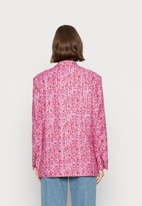 Blazer rose à motif floral avec une coupe légèrement oversize, manches longues et col à revers. Tissu texturé avec des fentes sur les côtés.