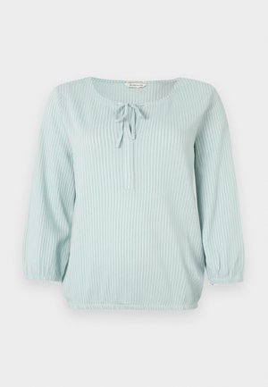 Heleheline pikkade varrukatega pluus, millel on valged vertikaalsed triibud, ümmargune kaelus, ees seotud detail ja elastsed mansetid ning ääred.