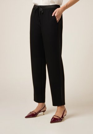 Pantalon de jogging noir avec taille élastique, cordon de serrage et poches latérales. Tissu lisse au design droit, associé à des talons bordeaux.
