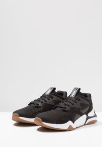 Schwarze Sportschuhe mit einem Obermaterial aus Mesh, Wildlederakzenten und einer Gummisohle. Zu den Merkmalen gehören ein gepolsterter Schaft und ein Schnürdesign.