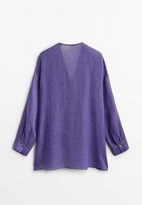 Blouse en lin violet avec col en V, manches longues et poignets boutonnés. Tissu léger et texturé avec une coupe décontractée.