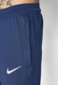 Navy athletic pants feature textured vertical stripes, an elastic waistband, side pocket, and a white Nike logo on the lower left thigh.