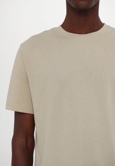 Camiseta de algodón beige con mangas cortas, cuello redondo y textura suave, con un diseño simple sin patrones ni embellimientos.