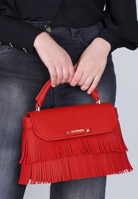 Borsa a tracolla in pelle rossa con dettagli in frangia, forma rettangolare e manico superiore. La ferramenta in metallo presenta una placca con logo sul davanti.
