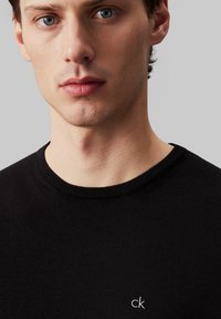 Svart bomulls t-skjorte med rund hals, med en liten "ck" logo på venstre bryst. Stoffet ser glatt ut med en tætsittende design.