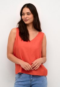 Ärmelloses Top mit V-Ausschnitt aus strukturiertem Korallstoff, mit einem lässigen Schnitt. Kombiniert mit hellblauen Jeans für einen entspannten Look.