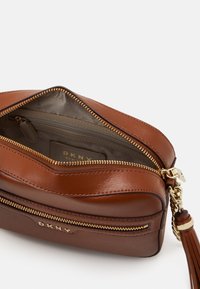 Brązowa skórzana torba na ramię z złotymi okuciami, zamkiem błyskawicznym i ozdobnym frędzlem. Posiada dwie przegrody, wyściełane wnętrze oraz wytłoczony logo.