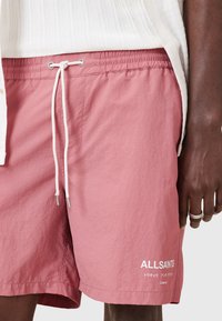 Lyserøde svøm shorts lavet af letvægtsstof. Har en elastisk talje med snor, sidelommer og hvidt logo detaljer.
