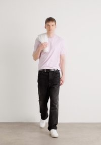 Lyserød kortærmet t-shirt, sorte lige ben jeans og hvide sneakers. Modellen bærer et hvidt håndklæde over skulderen.