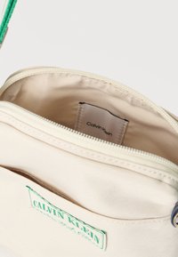 Μπεζ τσάντα καμβά Calvin Klein με πράσινο λογότυπο. Διαθέτει φερμουάρ, υφασμάτινη επένδυση και εσωτερική ετικέτα. Ομαλή υφή.
