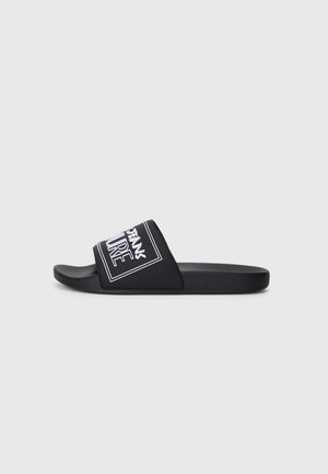 Svart glidesandal med en bred rem som har hvit tekst og rektangulært design. Teksturert såle og glatt removerflate.