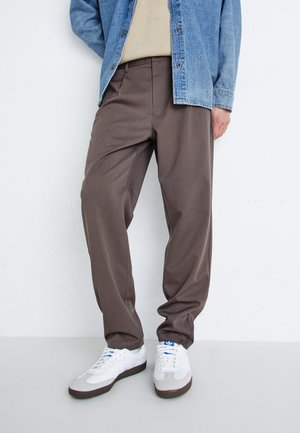 Brown relaxed-fit trousers with a smooth texture, paired with white sneakers. The outfit is complemented by a denim jacket and beige top.