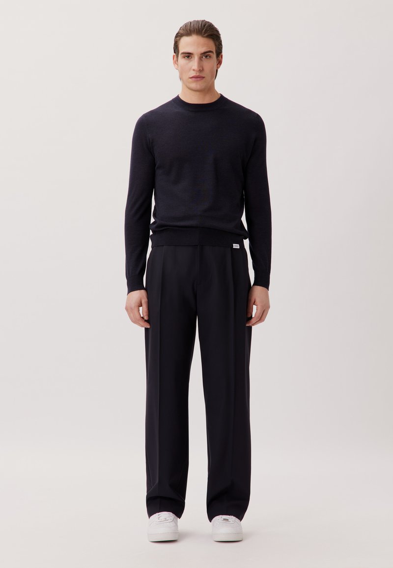 Un pull en maille bleu marine foncé, à encolure ronde ; associé à un pantalon large noir et des baskets blanches. Design minimaliste, sans motifs ni logos visibles.