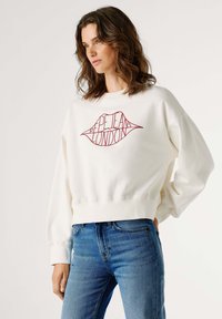 Sudadera blanca recortada con un gráfico de labios rojos y el texto "Pepe Jeans London". Cuenta con puños y dobladillo acanalados, y un ajuste relajado.