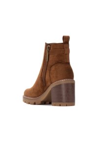 Stivaletto in suede marrone con zip laterale, linguetta sul tallone, tacco in legno spesso e suola in gomma texturizzata con scanalature.