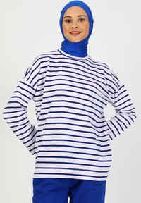 Maglietta bianca a maniche lunghe con righe orizzontali blu, caratterizzata da un taglio relax e scollatura a girocollo, indossata con un hijab blu abbinato.