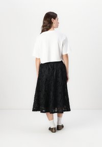 T-shirt blanc court, associé à une jupe midi noire avec des motifs texturés et superposés. Accessoirisé avec des chaussettes à la cheville et des ballerines à imprimé léopard.