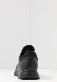 Czarne buty sportowe z teksturowaną cholewką, zaokrąglonym noskiem, wyściółką kołnierza i gumową podeszwą z ryflowanym wzorem dla lepszej przyczepności.
