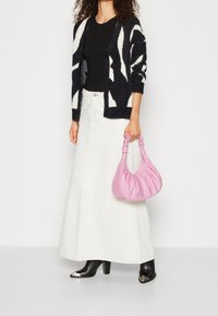 Černobílý vzorovaný chlupatý cardigan, černý top, bílá džínová sukně, černé kozačky na podpatku a růžová texturovaná kabelka s uzlovou rukojetí.