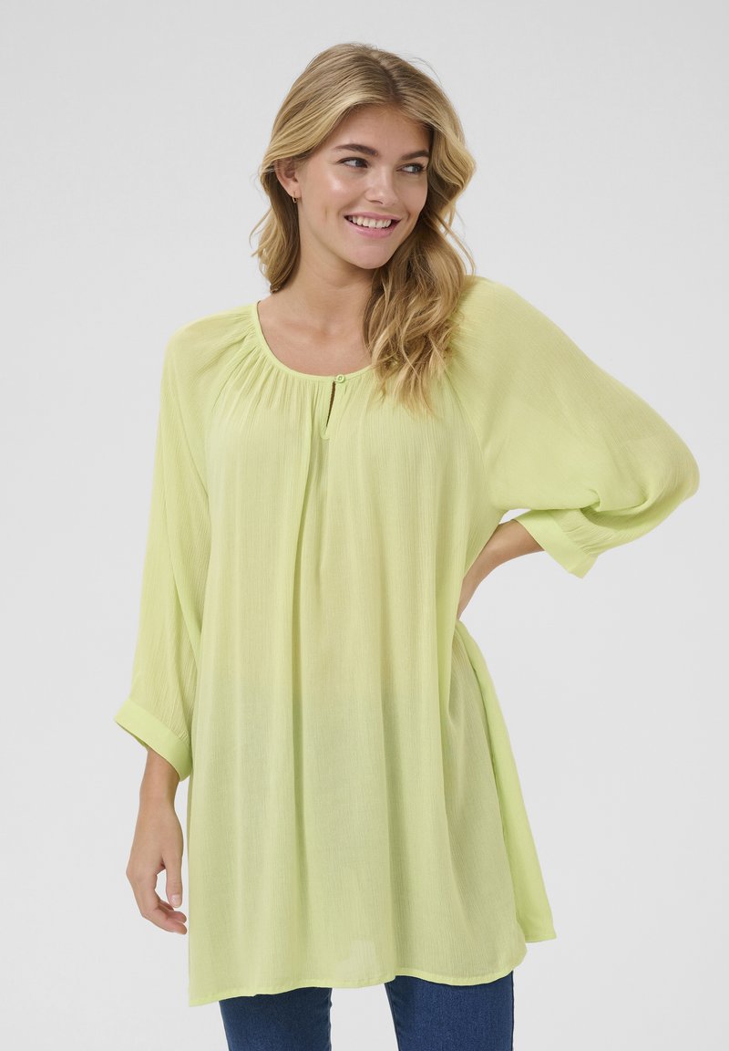 Tunique fluide, légère et transparente de couleur vert clair, avec des manches trois-quarts, un col froncé et un bouton unique sur le devant.