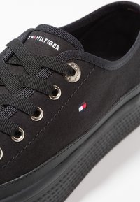 Schwarze Leinensneaker mit runder Spitze, strukturiertem Gummisohle, Metall-Ösen und schwarzen Schnürsenkeln. Verfügt über ein kleines rot-weiß-blaues Logo.
