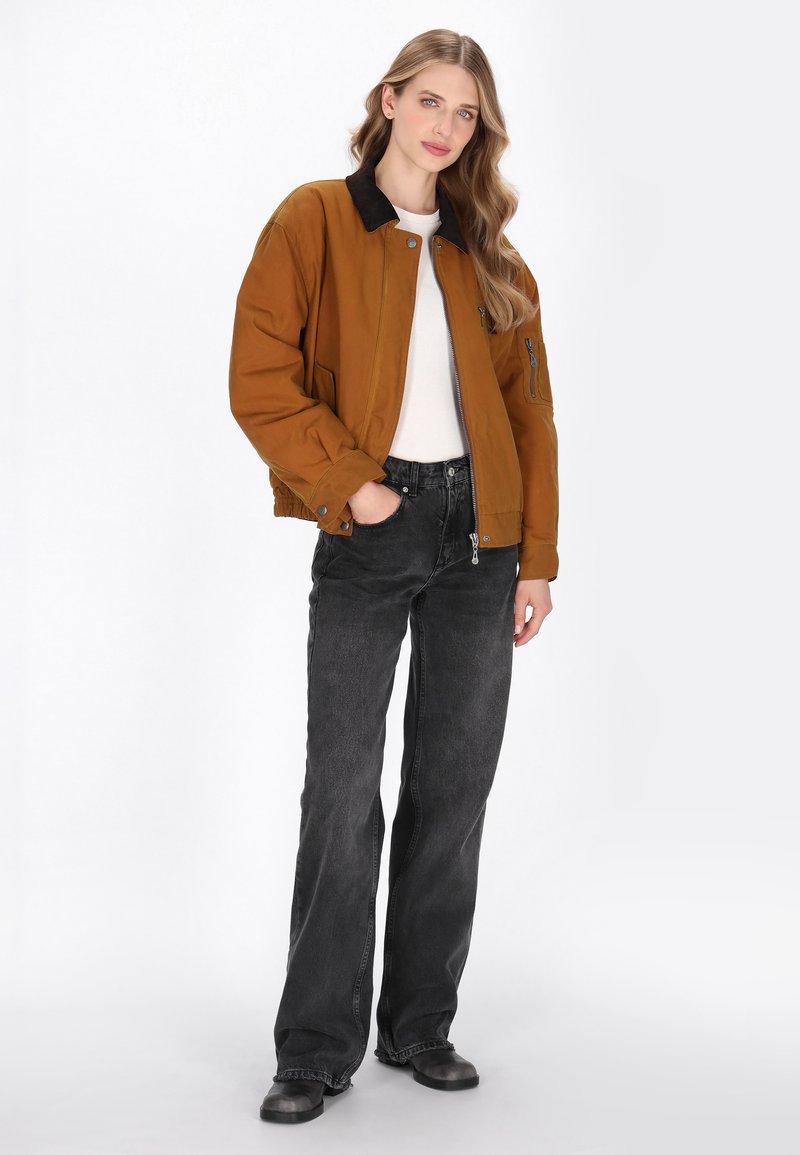 Brun bomberjakke med en sort krave, oversized pasform, lynlås lukning, parret med sorte wide-leg jeans og sorte støvler. Glat tekstur.