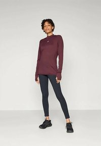 Burgunderfarget langermet topp med høy hals, sammen med svarte tights. Myk, elastisk stoff; tettsittende design. Har liten logo på brystet.