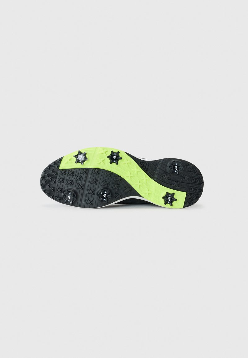 Schwarze Sport-Schuhsohle mit strukturiertem Muster, leuchtend gelben Akzenten und abnehmbaren schwarzen Stollen, die für Traktion auf Grasflächen ausgelegt sind.
