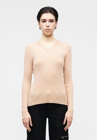 Pull à col en V à manches longues dans un doux pastel pêche avec une texture côtelée. Associé à un pantalon cargo foncé, doté de poches et de fermetures éclair.