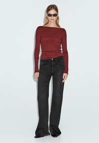 Top a maniche lunghe a righe rosse e nere, abbinato a jeans neri a vita alta e svasati. Modella con occhiali da sole neri di piccole dimensioni.