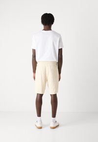 Light beige shorts with a textured pattern, feature a back pocket, worn with a plain white T-shirt and white sneakers with light soles.