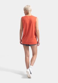 Haut sans manches orange en coton doux, avec un col rond et un petit logo sur le haut du dos. À porter avec des shorts.