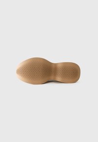 Semelle de chaussure marron avec des motifs de grip texturés, vue par le dessous sur un fond clair uni.