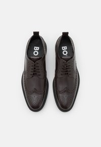 Chaussures habillées en cuir marron avec détails brogue, bout rond et semelle en caoutchouc noire. Lacets et languette au talon pour un enfilage facile.