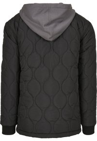 Veste matelassée noire avec coutures courbes et capuche grise attachée, vue de dos avec manches longues et poignets côtelés.