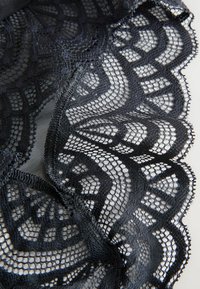 Melna mežģīņu auduma ar sarežģītiem ziedu un ģeometriskiem rakstiem, ar viļņotām malām un caurspīdīgu tekstūru.