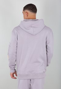 Svetlofialová mikina z mäkkej tkaniny, s veľkou kapucňou, rebrovanými manžetami a vreckom na ľavom rukáve. Hladká textúra.