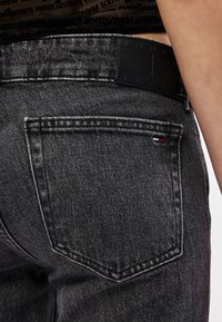 Tmavomodré džínsové nohavice s vreckom na zadnej strane zdobeným prešívaním a čiernou koženou záplatou s vyrazeným názvom značky. Červené, biele a modré akcenty.