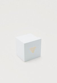 Witte kubusvormige Guess-merkkast met gouden logo in het midden op een effen witte achtergrond, met een zachte schaduw.