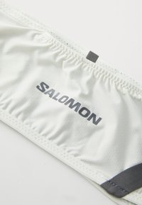 Fehér sportderékpánt rugalmas kialakítással, texturált felülettel és szürke "SALOMON" márkázással. Ráncolt varrás és hurok található rajta.