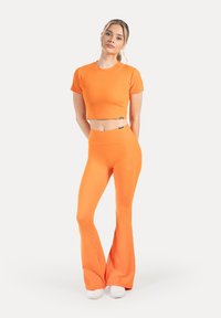 Haut court orange et leggings évasés, tous deux en matière extensible. La tenue présente un marquage minimal et une finition lisse de couleur unie.