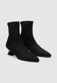 Bottines noires en daim souple avec un bout pointu et un talon sculptural unique. Présentent un design sans couture et un ajustement serré.